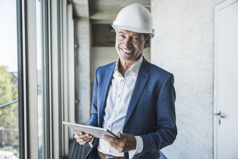 Glücklicher Ingenieur, der einen Tablet-PC in der Hand hält und im Korridor steht - UUF30652