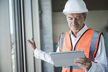 Lächelnder leitender Ingenieur mit Tablet-PC am Fenster - UUF30653