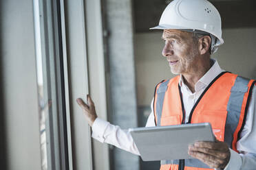 Ingenieur hält Tablet-PC und schaut durch das Fenster - UUF30654