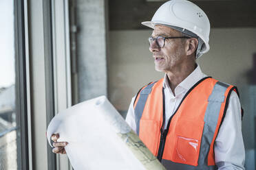 Nachdenklicher Ingenieur mit Schutzhelm und Blaupause am Fenster - UUF30656