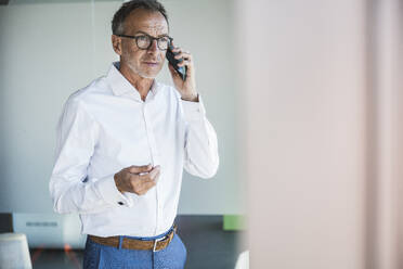 Geschäftsmann, der im Büro mit seinem Smartphone telefoniert - UUF30665