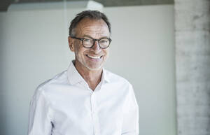 Happy senior businessman wearing eyeglasses in office - UUF30667