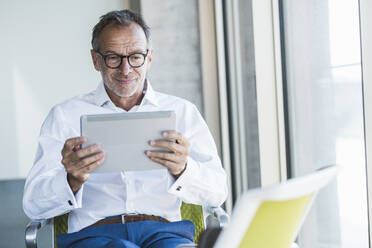 Smiling businessman using tablet PC in office - UUF30673