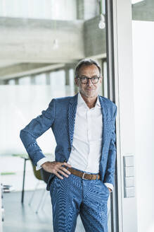 Smiling businessman leaning on wall in office doorway - UUF30676