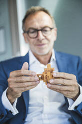 Businessman holding wooden toy blocks in office - UUF30684