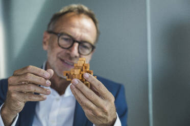 Lächelnder Geschäftsmann hält Holzspielzeugblöcke im Büro - UUF30685