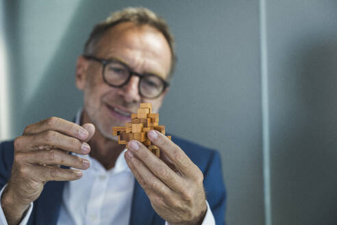 Smiling businessman holding wooden toy blocks in office - UUF30685