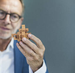 Businessman examining toy blocks against gray background - UUF30688