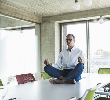 Businessman with eyes closed meditating on desk in office - UUF30704