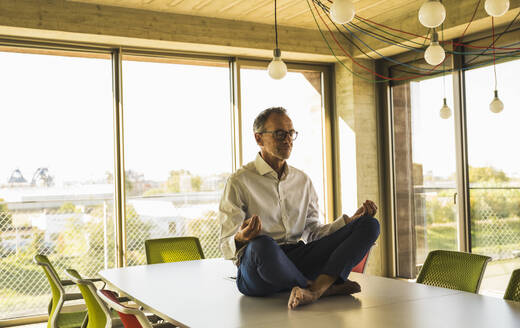 Senior businessman meditating on conference table - UUF30706