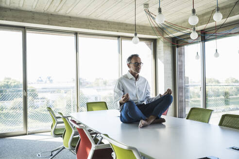 Senior businessman meditating on conference table in office - UUF30707
