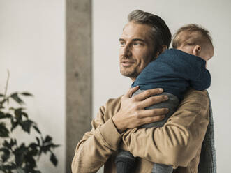 Mature man carrying baby boy near wall at home - MFF09506