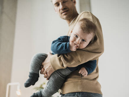 Man holding baby boy in front of wall at home - MFF09514