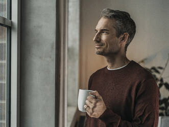 Thoughtful man holding coffee cup at home - MFF09520