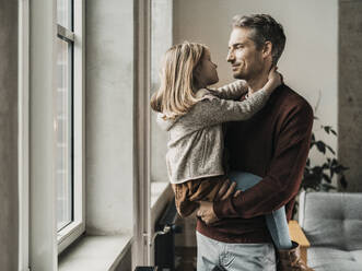 Lächelnder Vater, der seine Tochter in den Armen hält, in der Nähe des Fensters zu Hause - MFF09523