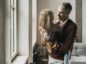 Man standing near window with daughter at home - MFF09524