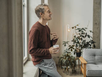 Man holding coffee cup and gesturing at home - MFF09532