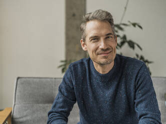 Lächelnder Mann mit blauem T-Shirt, der zu Hause sitzt - MFF09542