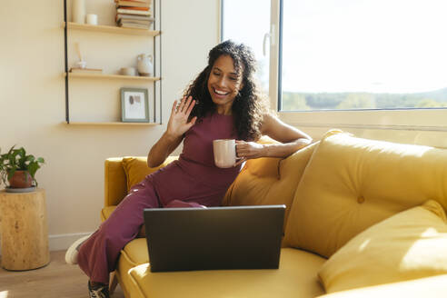Lächelnde Geschäftsfrau bei einer Videokonferenz mit Laptop auf dem Sofa im Büro - EBSF04087