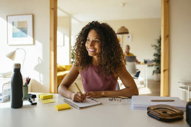 Lächelnde Geschäftsfrau mit Stift und Notizblock auf dem Schreibtisch im Büro - EBSF04101