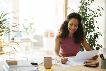 Lächelnde Geschäftsfrau bei der Arbeit an Dokumenten am Schreibtisch im Büro - EBSF04108