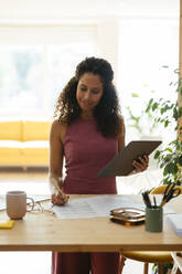 Smiling businesswoman taking notes from tablet PC at desk in office - EBSF04115