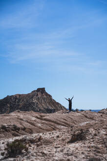 Junge Frau mit erhobenen Armen vor einem Berg unter blauem Himmel stehend - RSGF00974