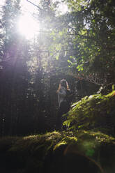 Woman with backpack hiking in forest on sunny day - RSGF00982
