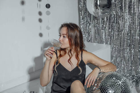 Frau trinkt Champagner in der Nähe der Discokugel auf einer Weihnachtsfeier - ADF00265