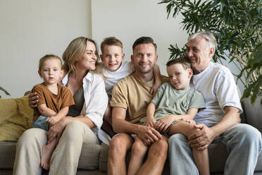 Happy multi-generational family sitting on sofa in living room at home - SVKF01707