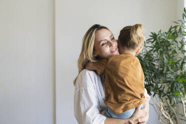 Smiling blond mother carrying boy at home - SVKF01713