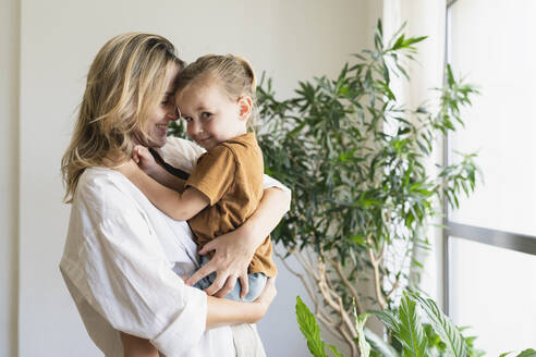 Lächelnde Mutter umarmt und trägt süßen Jungen zu Hause - SVKF01714