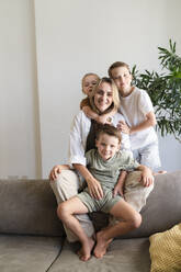 Smiling mother with three sons sitting on sofa at home - SVKF01725