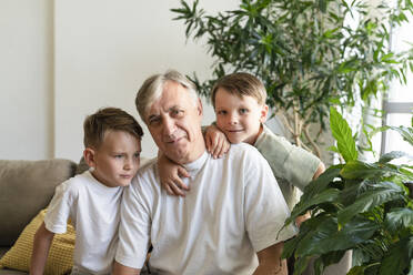 Senior man sitting with grandsons in living room at home - SVKF01729