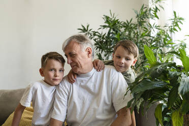 Senior man sitting with grandsons on sofa at home - SVKF01730