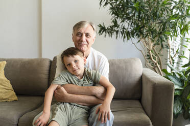 Großvater umarmt seinen Enkel auf dem Sofa zu Hause - SVKF01733