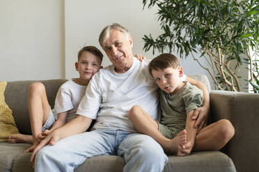 Lächelnder älterer Mann sitzt zusammen mit Jungen auf dem Sofa zu Hause - SVKF01734