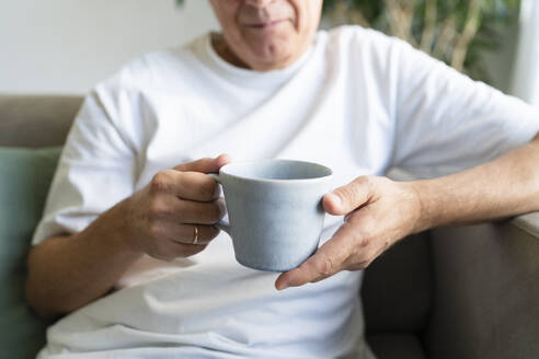 Älterer Mann hält Kaffeetasse im Wohnzimmer zu Hause - SVKF01748