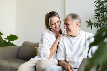 Lächelnde Tochter und Vater sitzen zusammen im Wohnzimmer zu Hause - SVKF01754