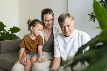 Senior man sharing laptop with daughter and grandson at home - SVKF01756