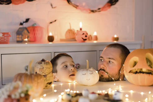 Vater und Sohn schauen sich in der Nähe von Halloween-Dekoration auf dem Tisch an - ONAF00709