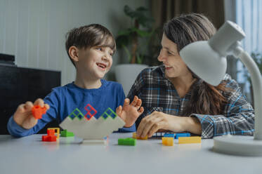 Happy mother and son playing with toy blocks at home - ANAF02494