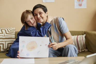 Smiling mother and her daughter with Down syndrome showing drawing - KPEF00416