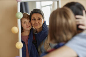 Mutter und jugendliche Tochter mit Down-Syndrom betrachten sich im Spiegel - KPEF00423