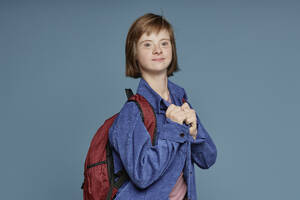 Jugendlicher mit Behinderung trägt Rucksack vor blauem Hintergrund - KPEF00443