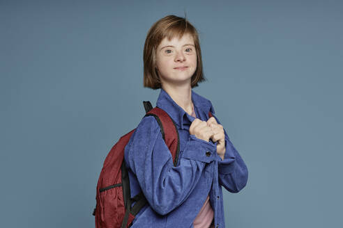 Teenager with disability wearing backpack against blue background - KPEF00443