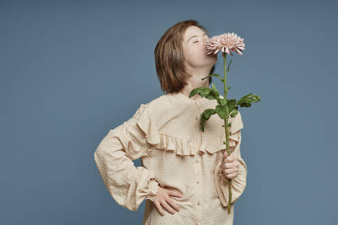 Teenage girl smelling at crown daisy standing against blue background - KPEF00451