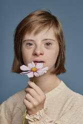 Girl with Down syndrome holding pink flower against blue background - KPEF00456