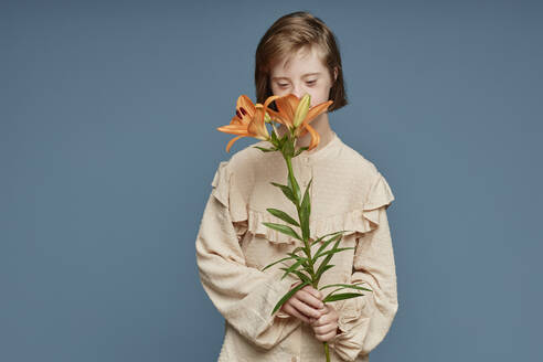 Teenage girl smelling orchid flowers standing against blue background - KPEF00457