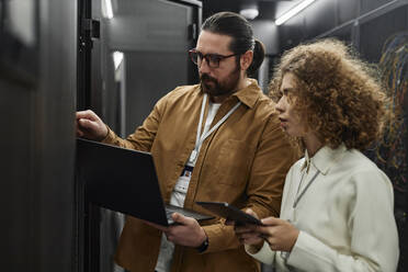 IT professionals examining servers with laptop and tablet PC in data center - KPEF00485